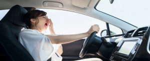 Une jeune femme en train de bailler en conduisant une voiture