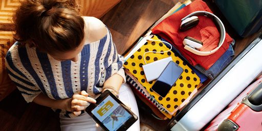 Une jeune femme en train de préparer sa valise avec des objets high-tech pour aller en vacances